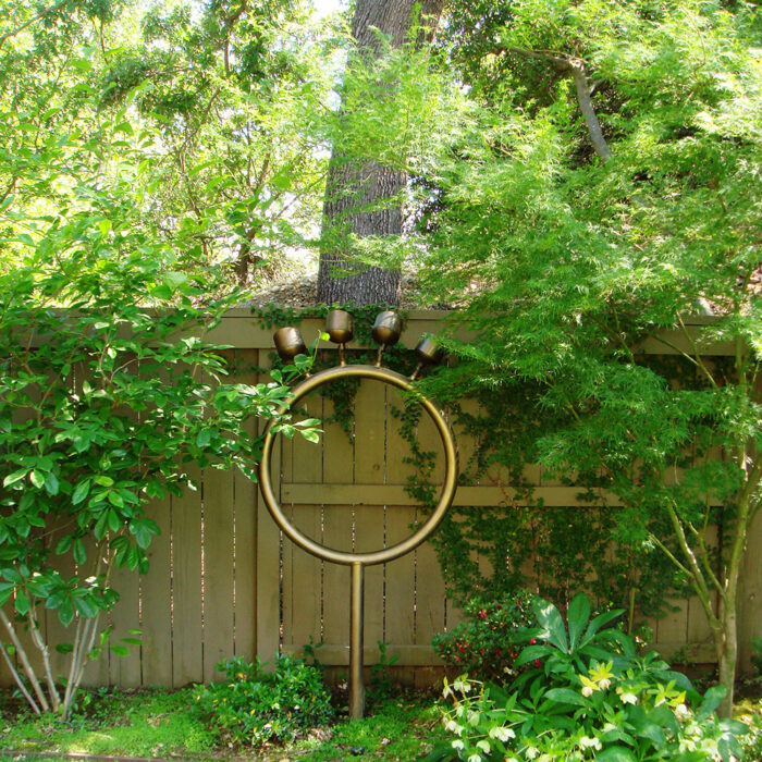 an image of a custom lighting installation that looks like a gold ring with four protruding lights on top of it pointing up at the trees